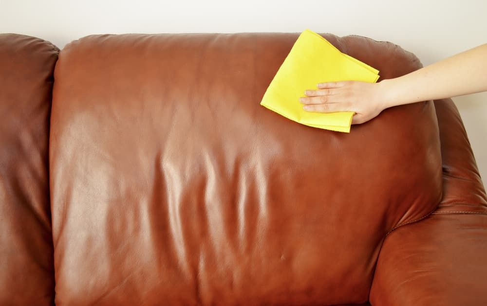 A Person Is Cleaning a Brown Leather Couch — Complete Clean Home Cleaning in Warrawong, NSW