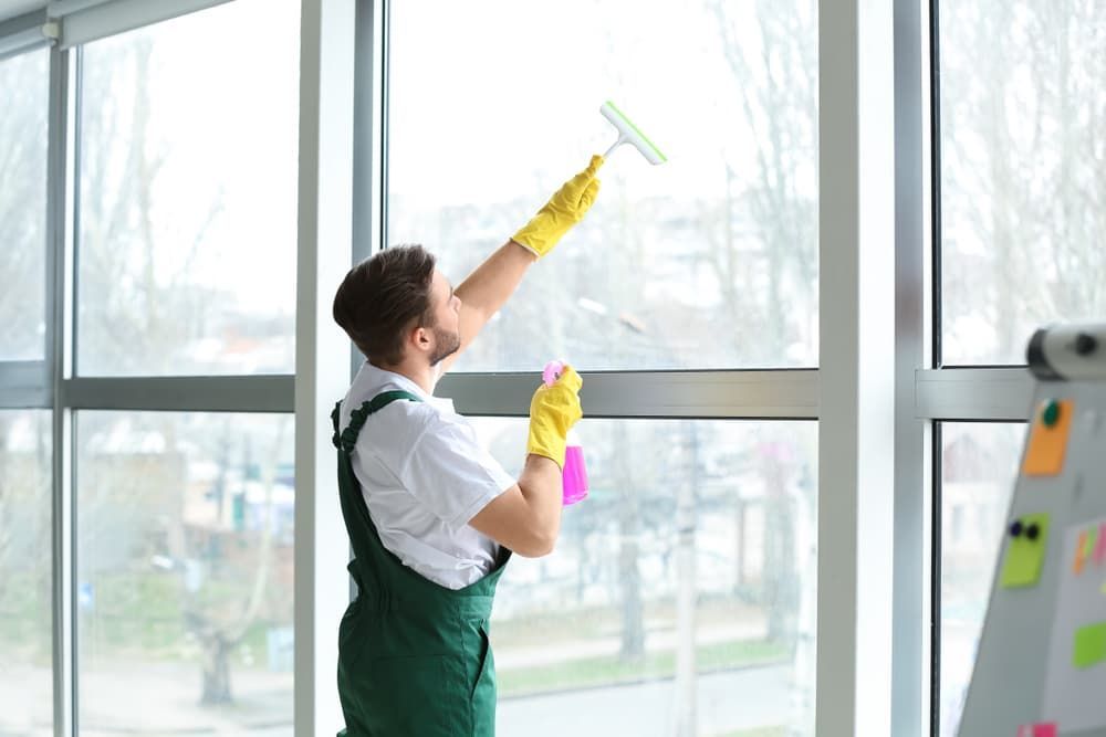 A Man Is Cleaning a Window with A Squeegee — Complete Clean Home Cleaning in Albion Park, NSW