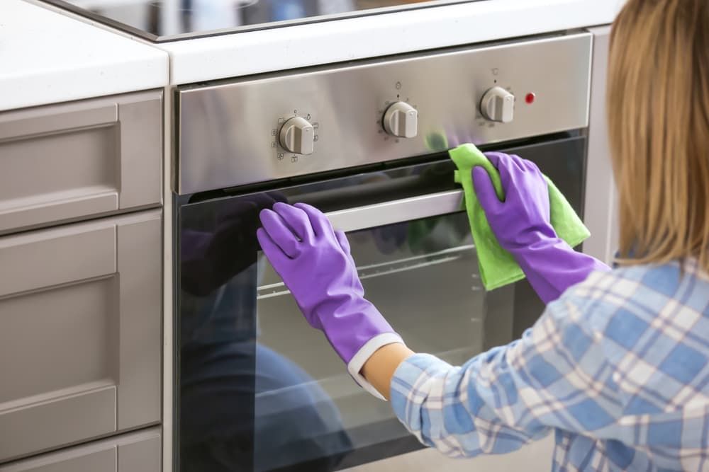 A Woman Wearing Purple Gloves Is Cleaning an Oven — Complete Clean Home Cleaning in Shellharbour, NSW