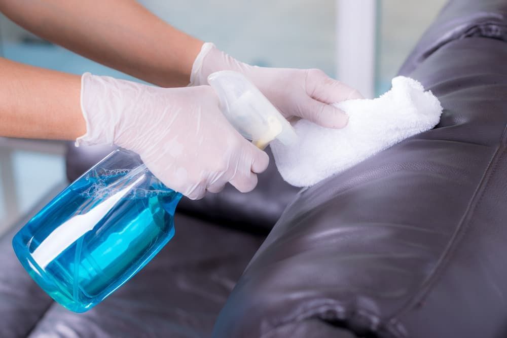A Person Is Cleaning a Leather Couch with A Spray Bottle — Complete Clean Home Cleaning in Warrawong, NSW