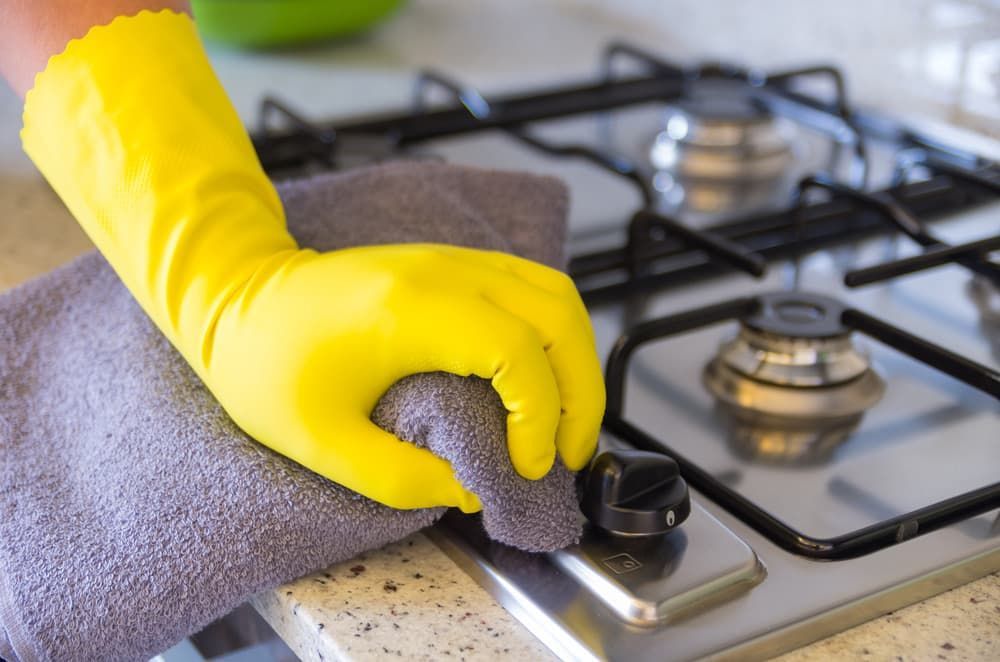 A Person Wearing Yellow Gloves Is Cleaning a Stove — Complete Clean Home Cleaning in Dapto, NSW