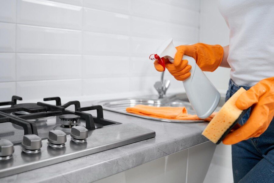 A Woman in Orange Gloves Is Cleaning a Kitchen Counter — Complete Clean Home Cleaning in Corrimal, NSW