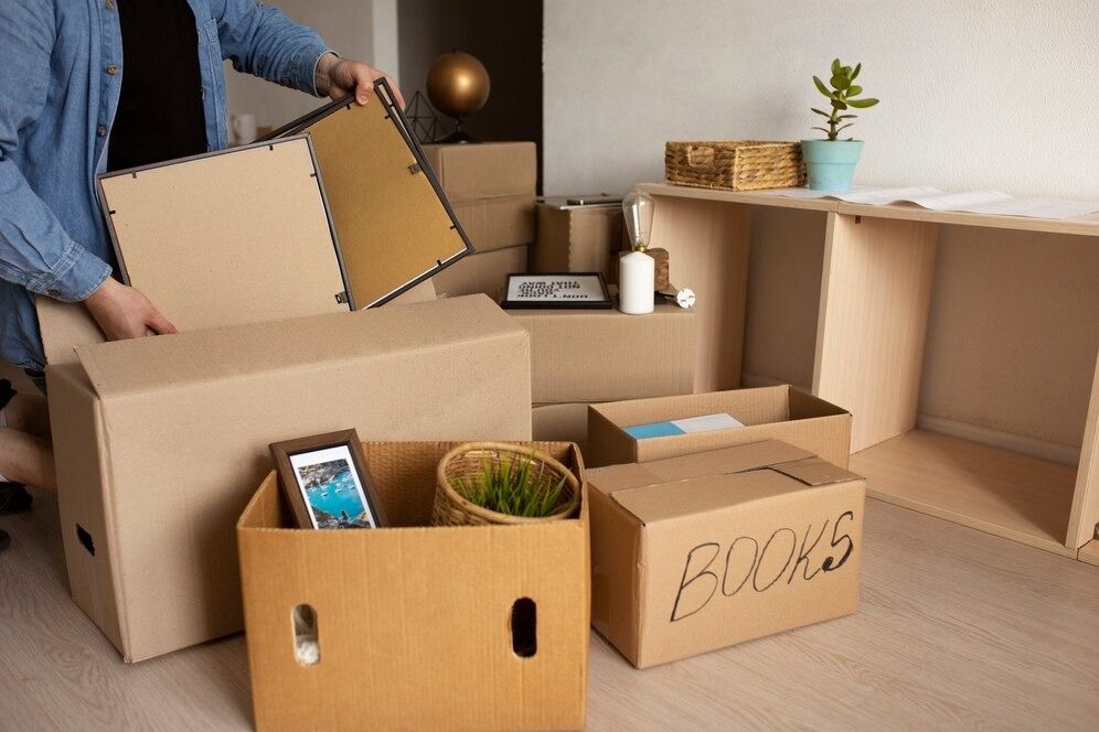 A Man Is Packing Boxes in A Living Room — Complete Clean Home Cleaning in Albion Park, NSW
