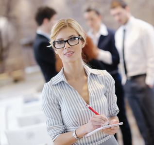 Three business professionals at a table. Woman smiles; man looks and smiles. A person faces them.