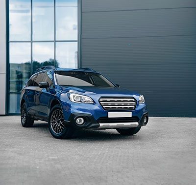 A blue subaru outback is parked in front of a building.