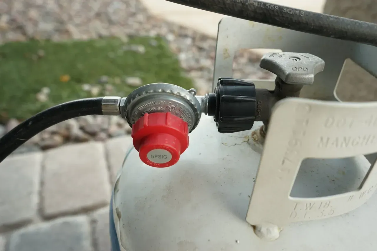 A propane tank with a red cap and a black hose attached to it