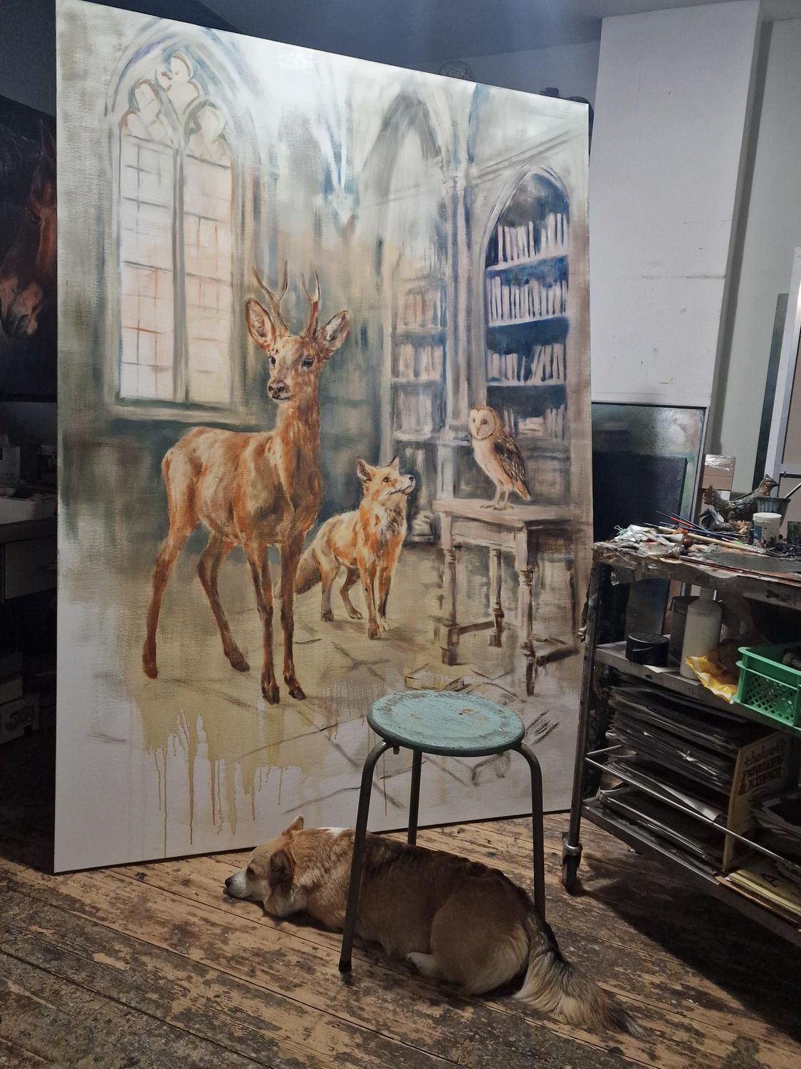 Een hond ligt op de grond voor een groot schilderij van herten.