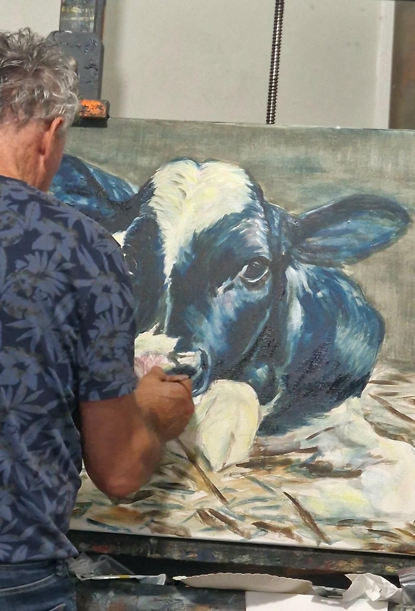 Een man schildert een zwart-witte koe op een doek.