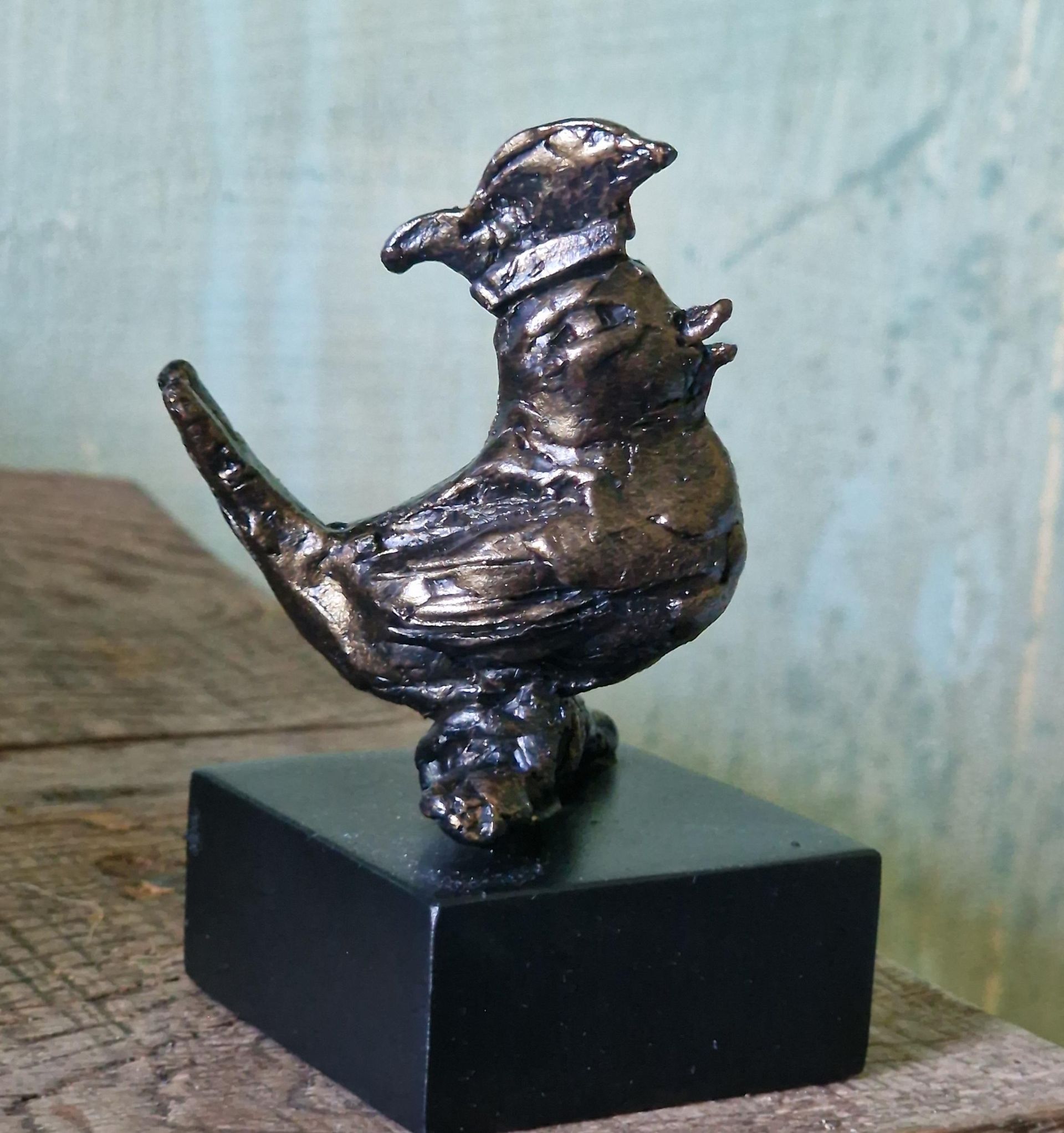 Een klein bronzen beeldje van een vogel op een zwarte sokkel