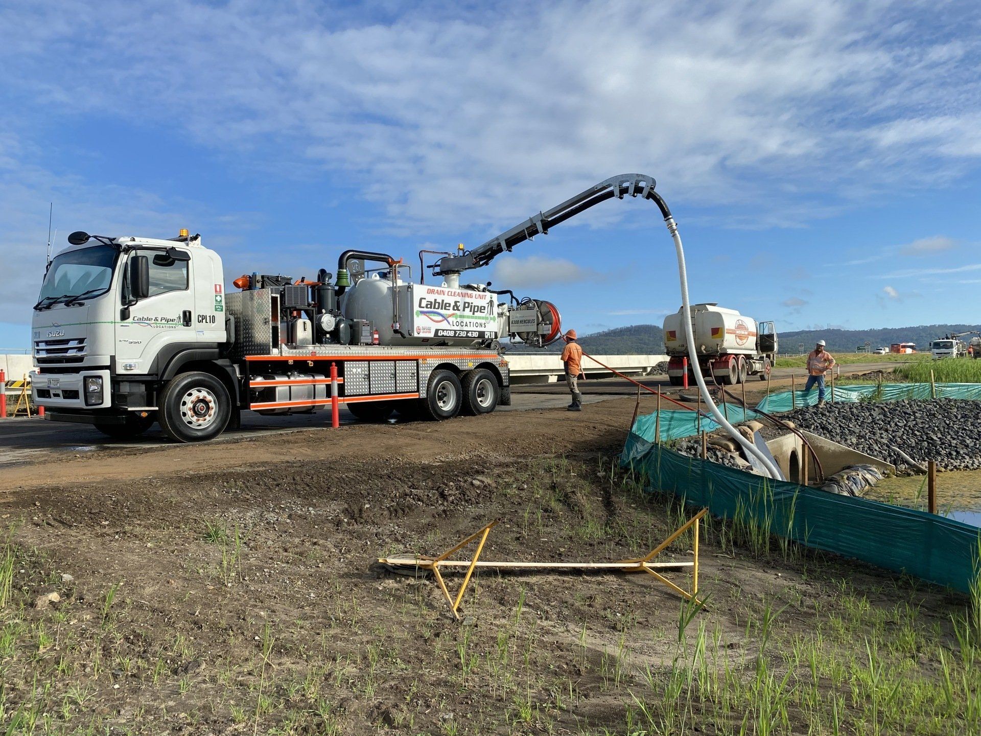 White truck with extended arm vaccuuming liquid from the ground at a construction site.