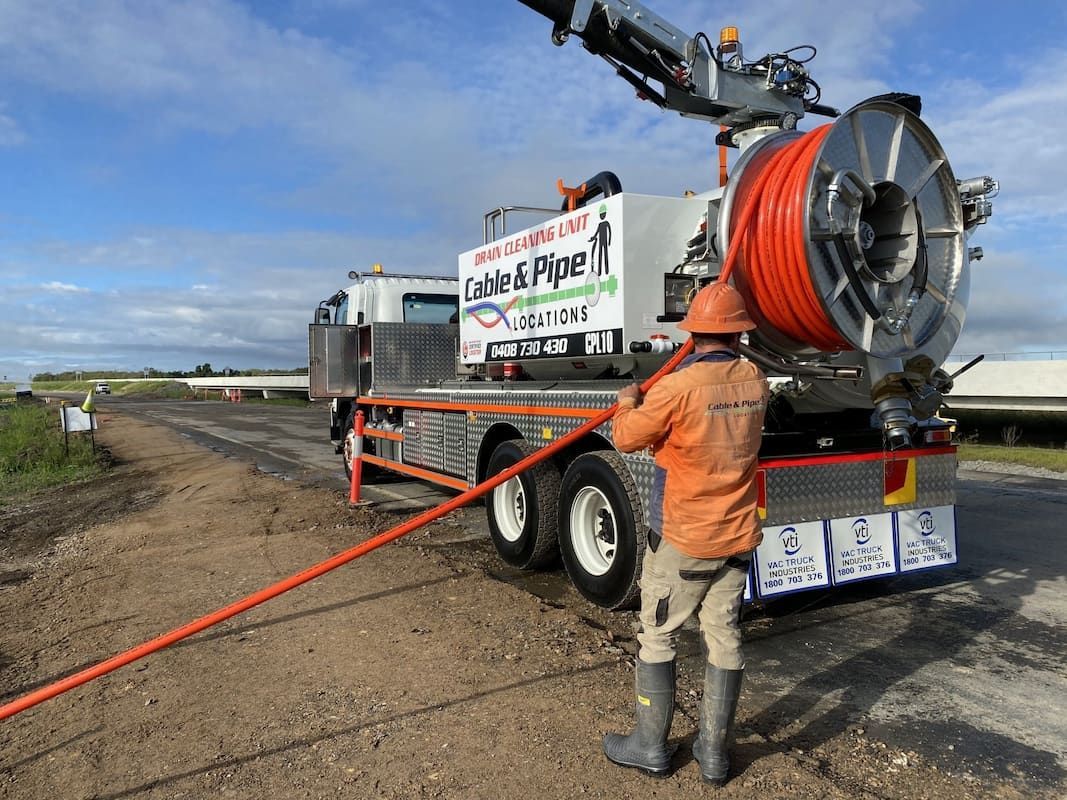 Worker Pulling Orange Pipe From Utility Truck On A Dirt Road, Under Cloudy Sky