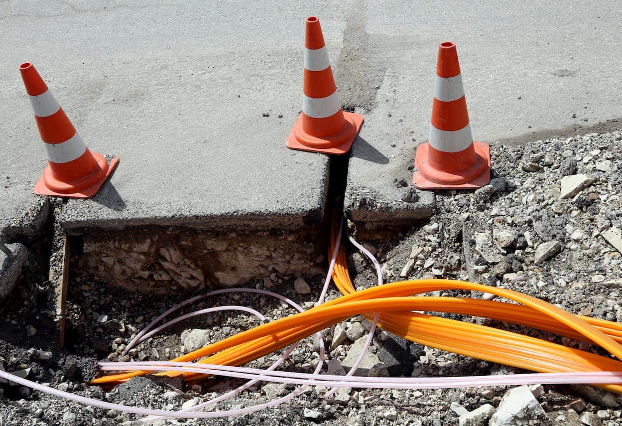 cable locating in progress during excavation, with orange conduits and safety cones marking dig site