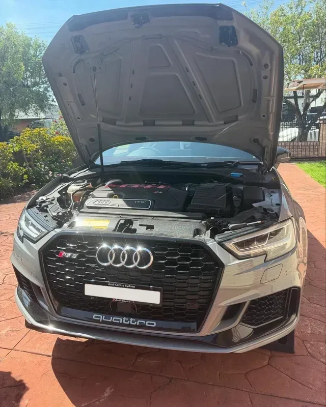 Gray Audi RS3 with hood open, parked on a red brick driveway, with a grassy yard and trees in the background — Amrix Automotive In Bankstown, NSW