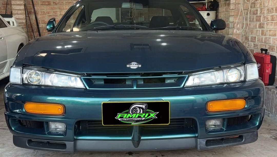 Dark teal Nissan S14 Silvia with rectangular headlights, orange turn signals, parked indoors — Amrix Automotive In Bankstown, NSW