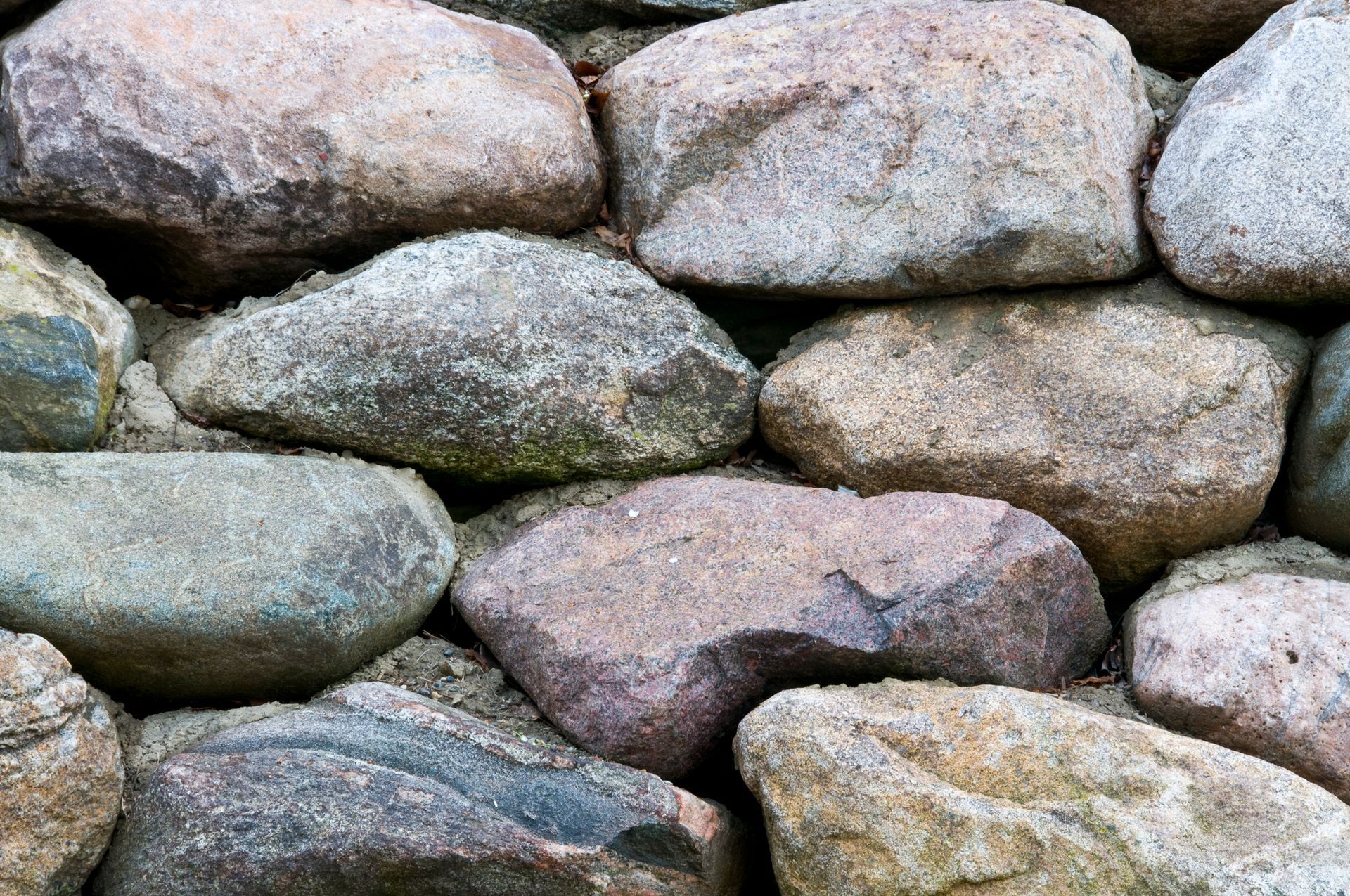 Close-up of a stacked stone wall made of various sized gray, brown, and pink rocks.