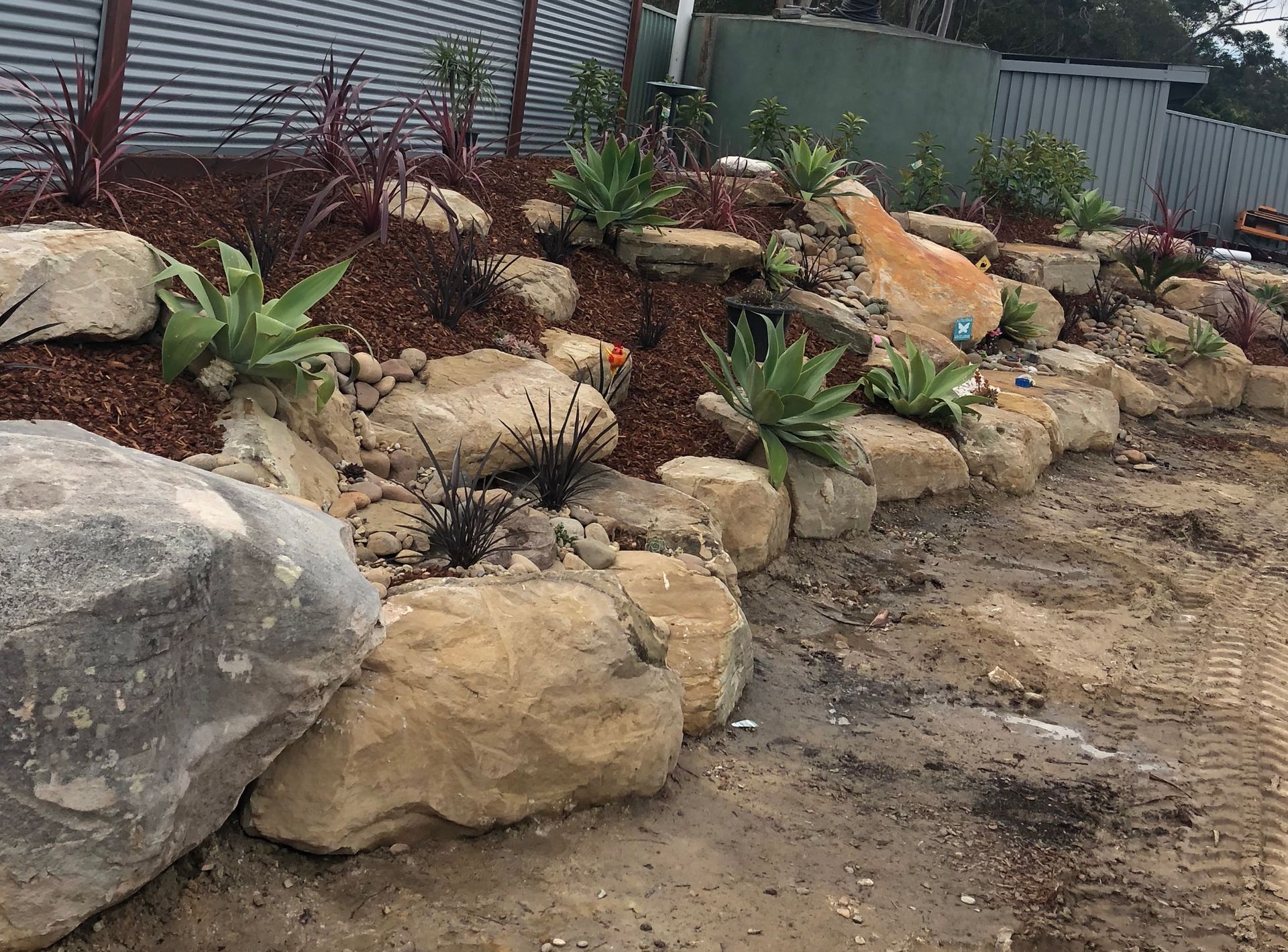 Rock retaining wall with plants and mulch; construction site.