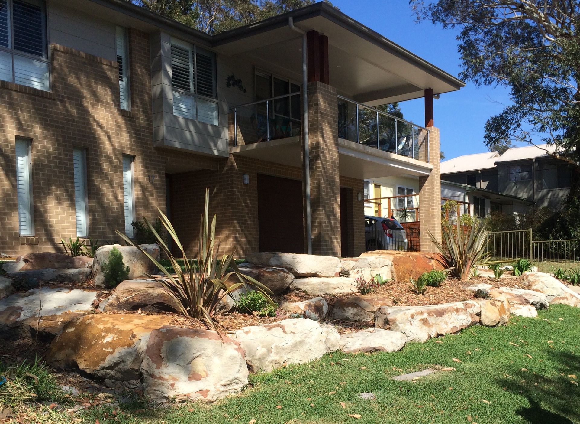 Two-story brick house with a stone landscape and balcony, with a green lawn and blue sky.