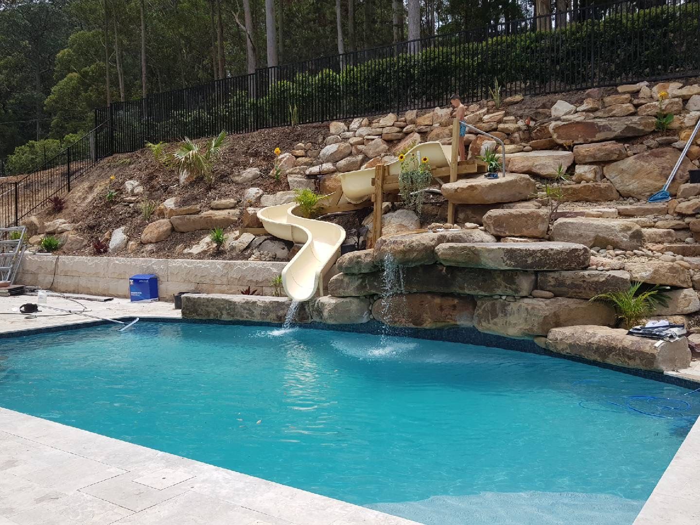 A pool with blue water and a slide built into a stone wall, with greenery.