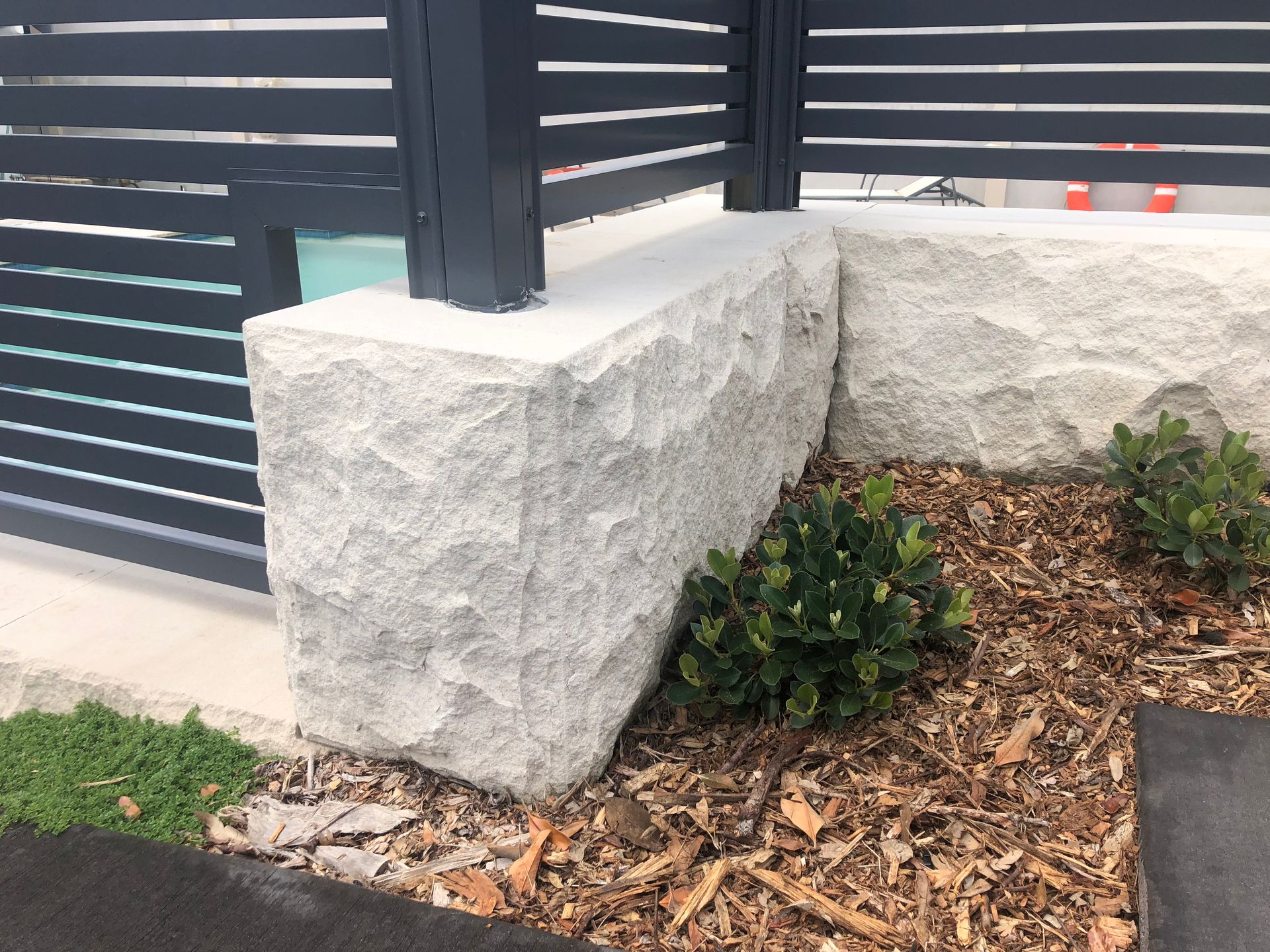 Stone pillars supporting a dark gray slatted fence with small green plants.