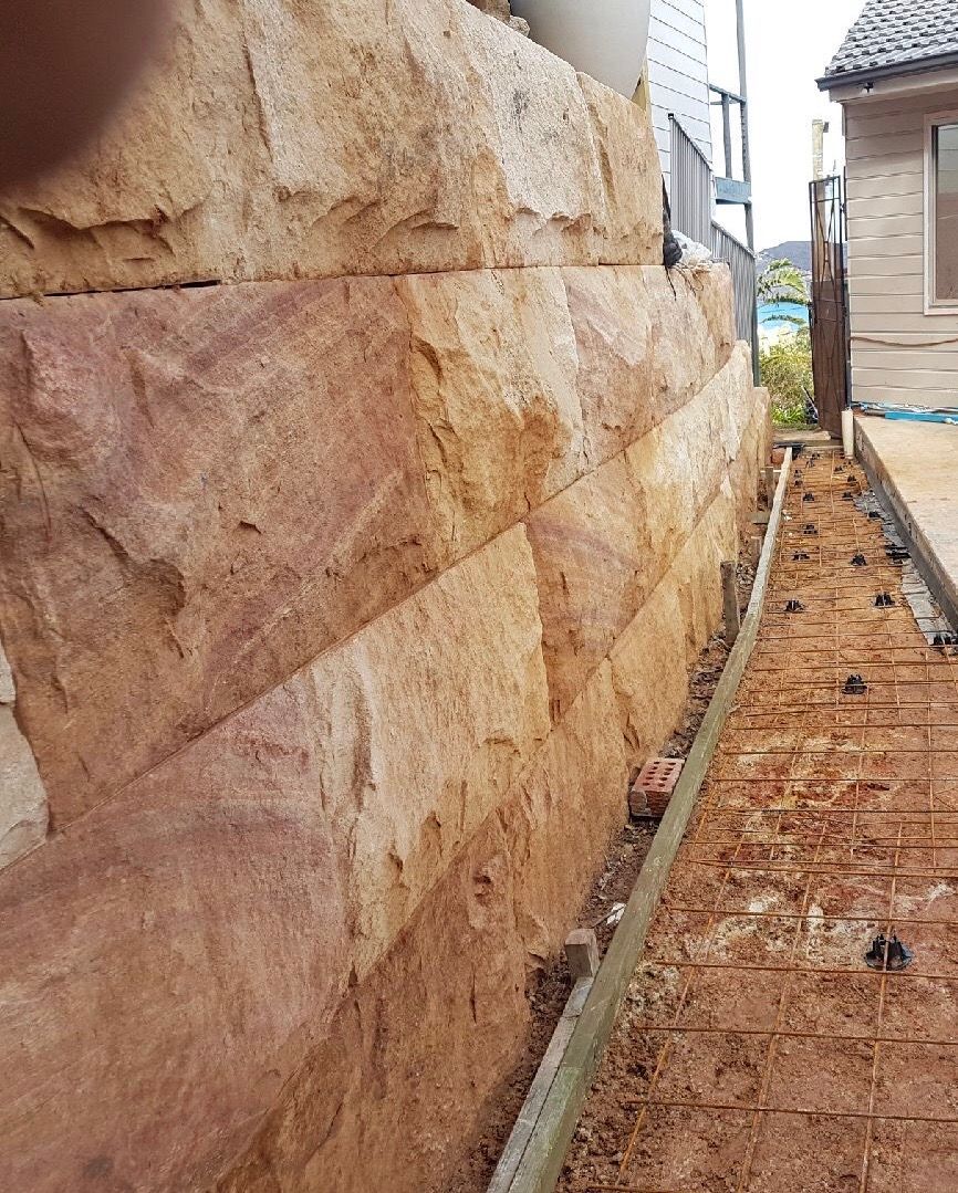 A reddish-brown sandstone retaining wall next to a concrete and rebar base.