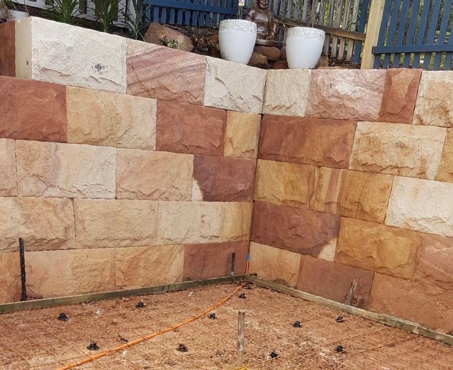 Sandstone retaining wall with two white pots on top.