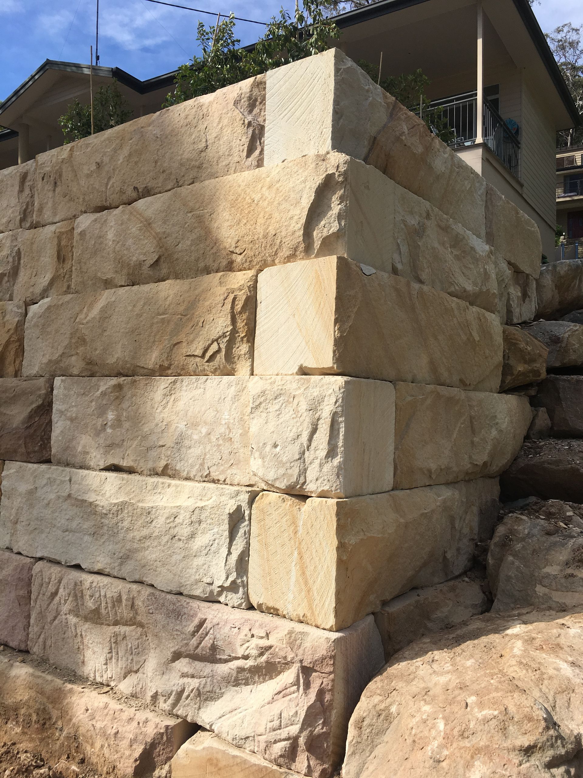 Sandstone retaining wall corner, built with large, rectangular blocks, against a house.