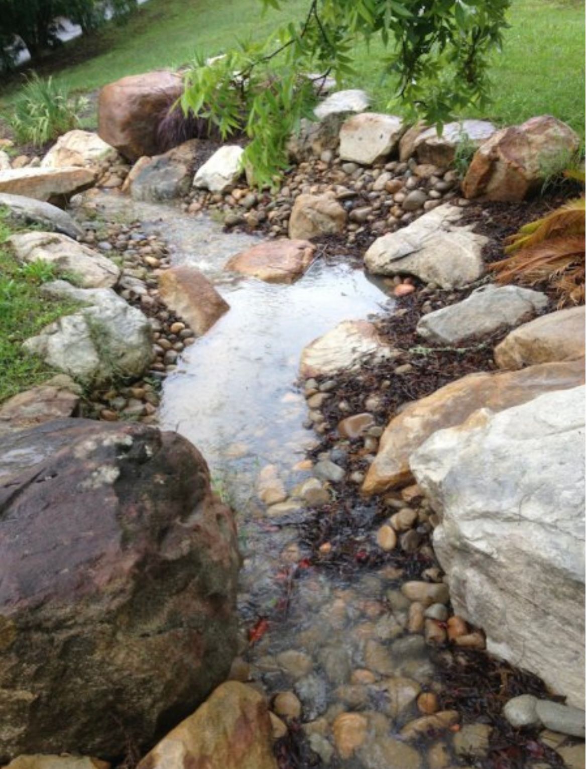 A small stream flows through rocks and gravel in a garden.