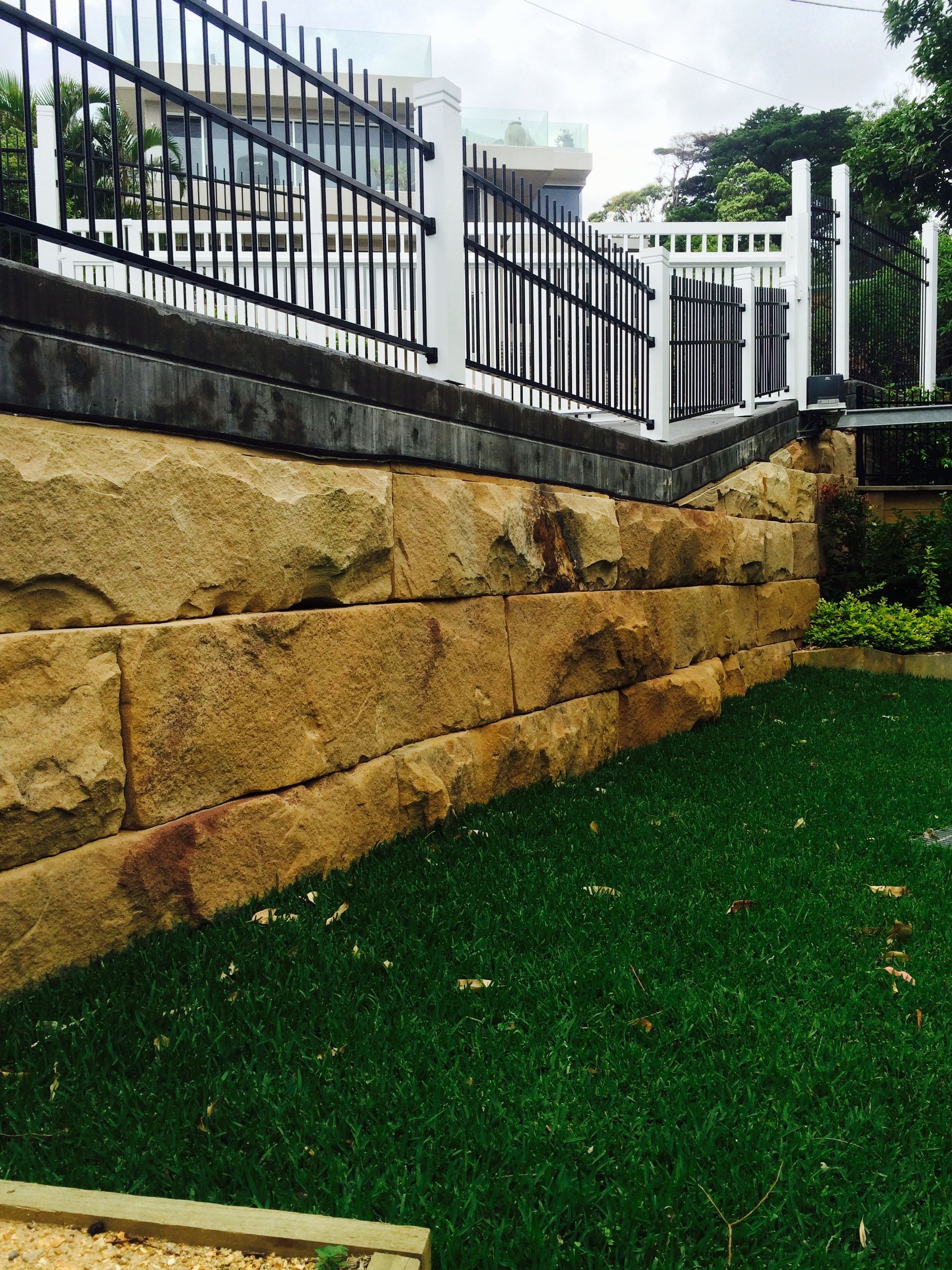 Stone retaining wall with a black and white fence, green lawn.
