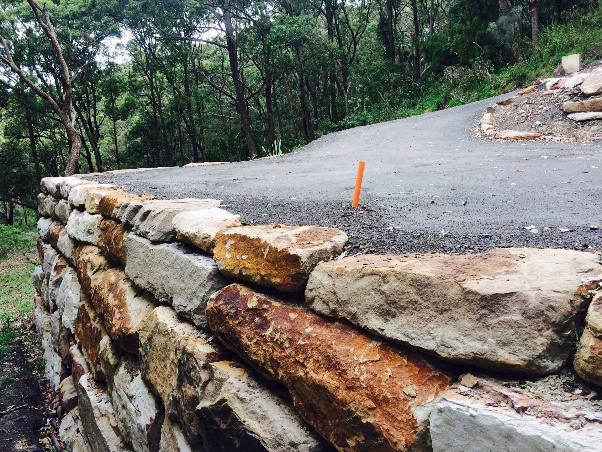 Stone retaining wall borders a paved road, forest in the background.