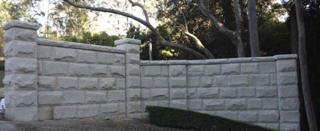 Stone wall with columns; trees in the background.