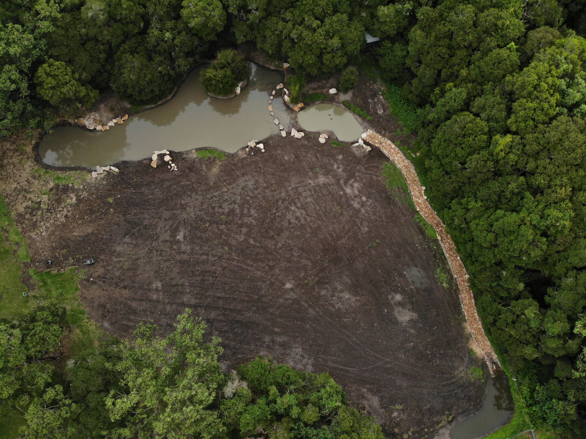 Aerial view of a dark dirt field and a pond surrounded by a forest.