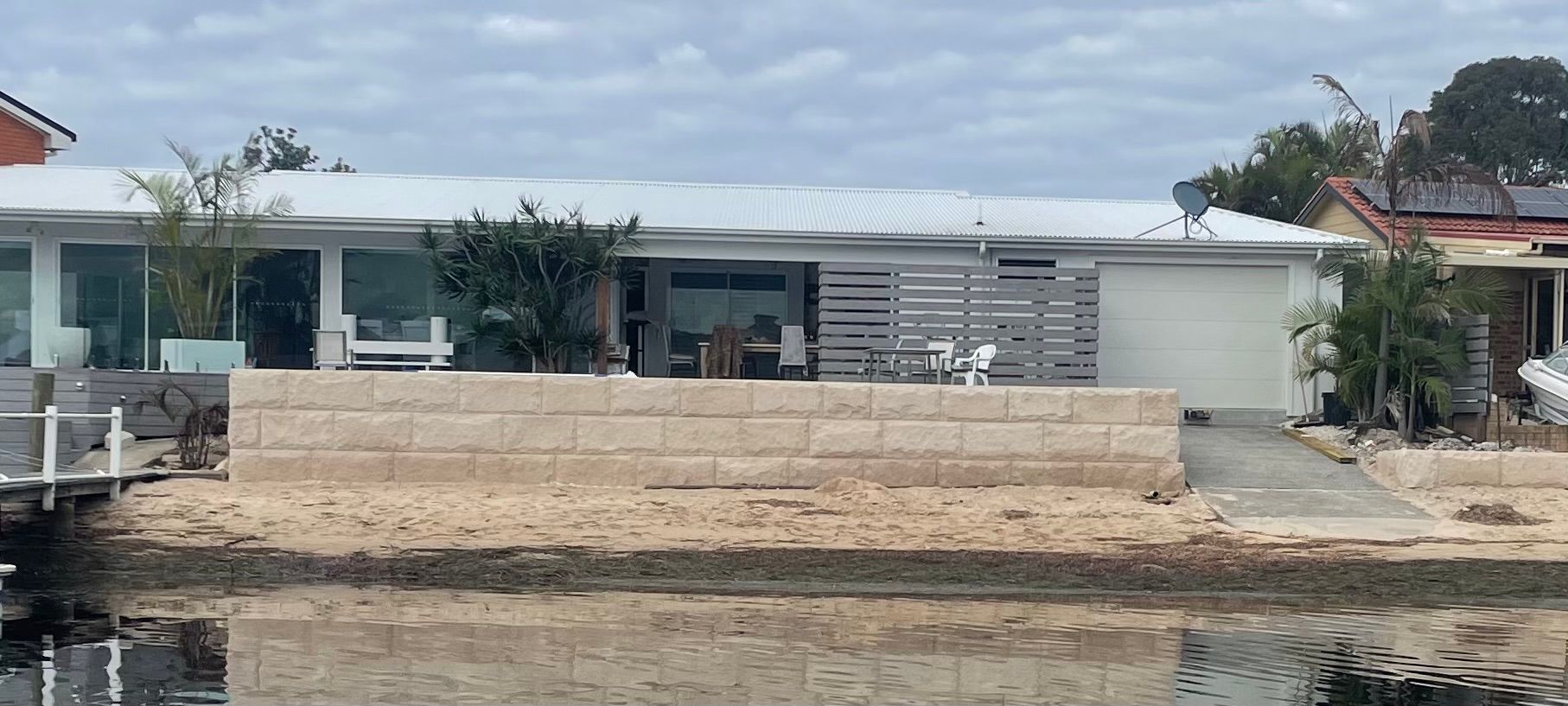 A waterfront house with a retaining wall, garage, and a pier, under a cloudy sky.
