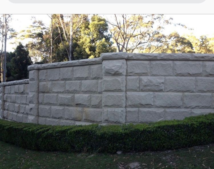 Stone wall with a green hedge in front, trees in the background.
