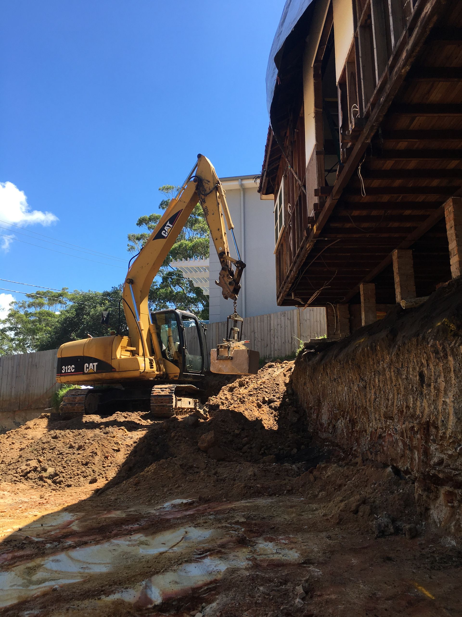 Yellow excavator placing a concrete block on a wall under construction outdoors.