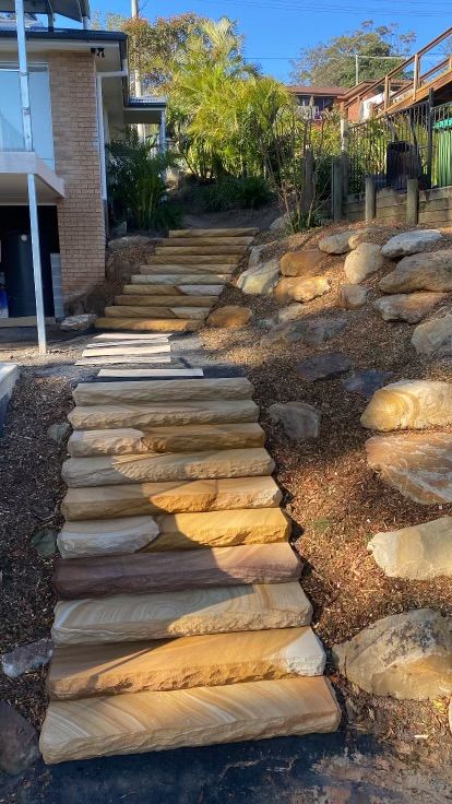 Stone steps lead uphill, surrounded by mulch and rocks, next to a building.