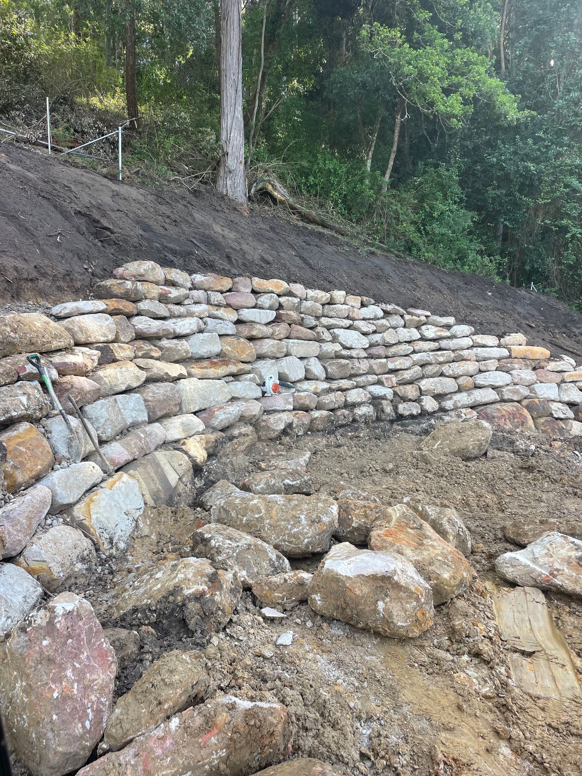 Stone retaining wall under construction on a hillside, using large, irregular stones.