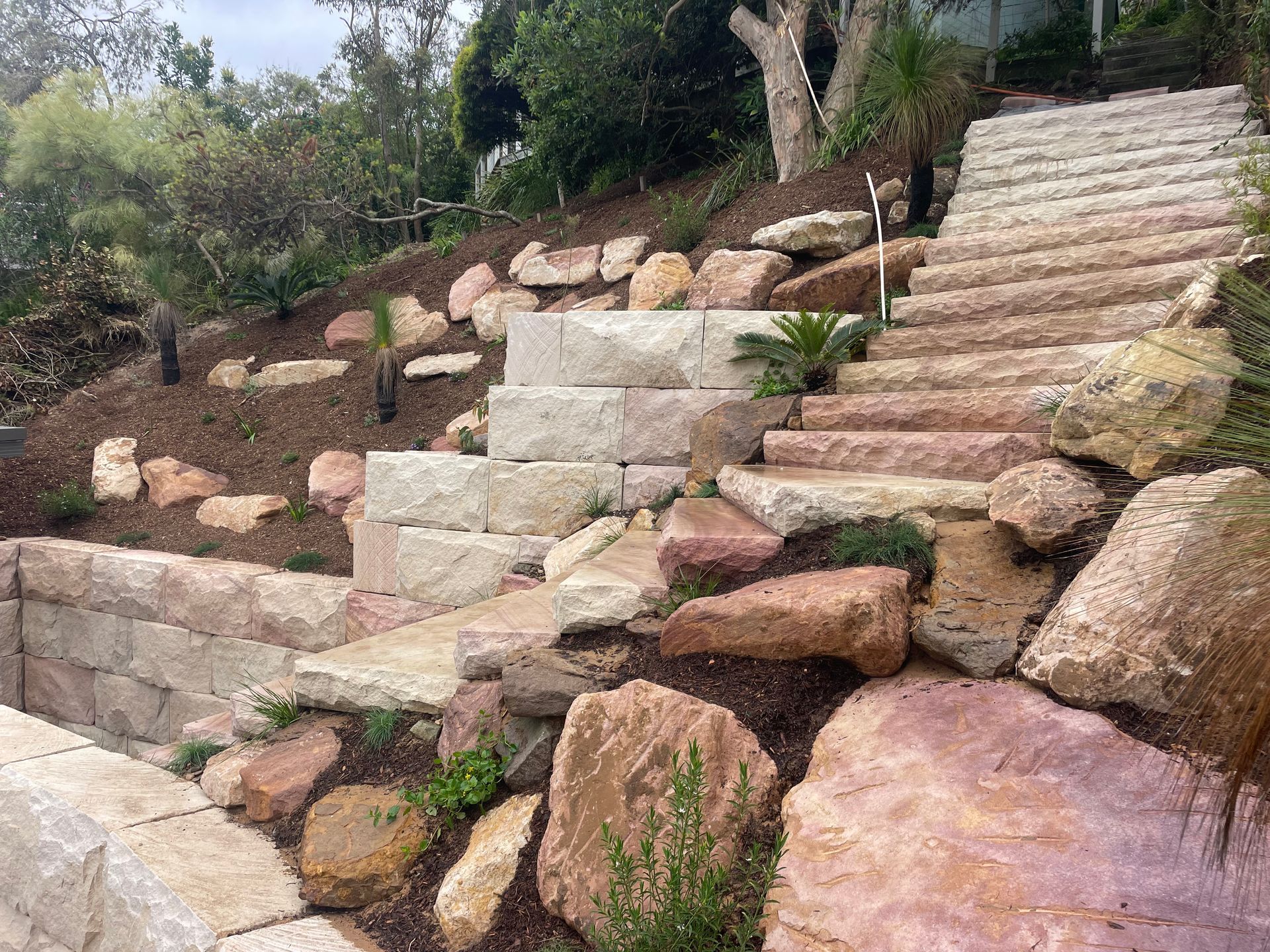 Stone steps and retaining walls built into a hillside garden with rocks and plants.