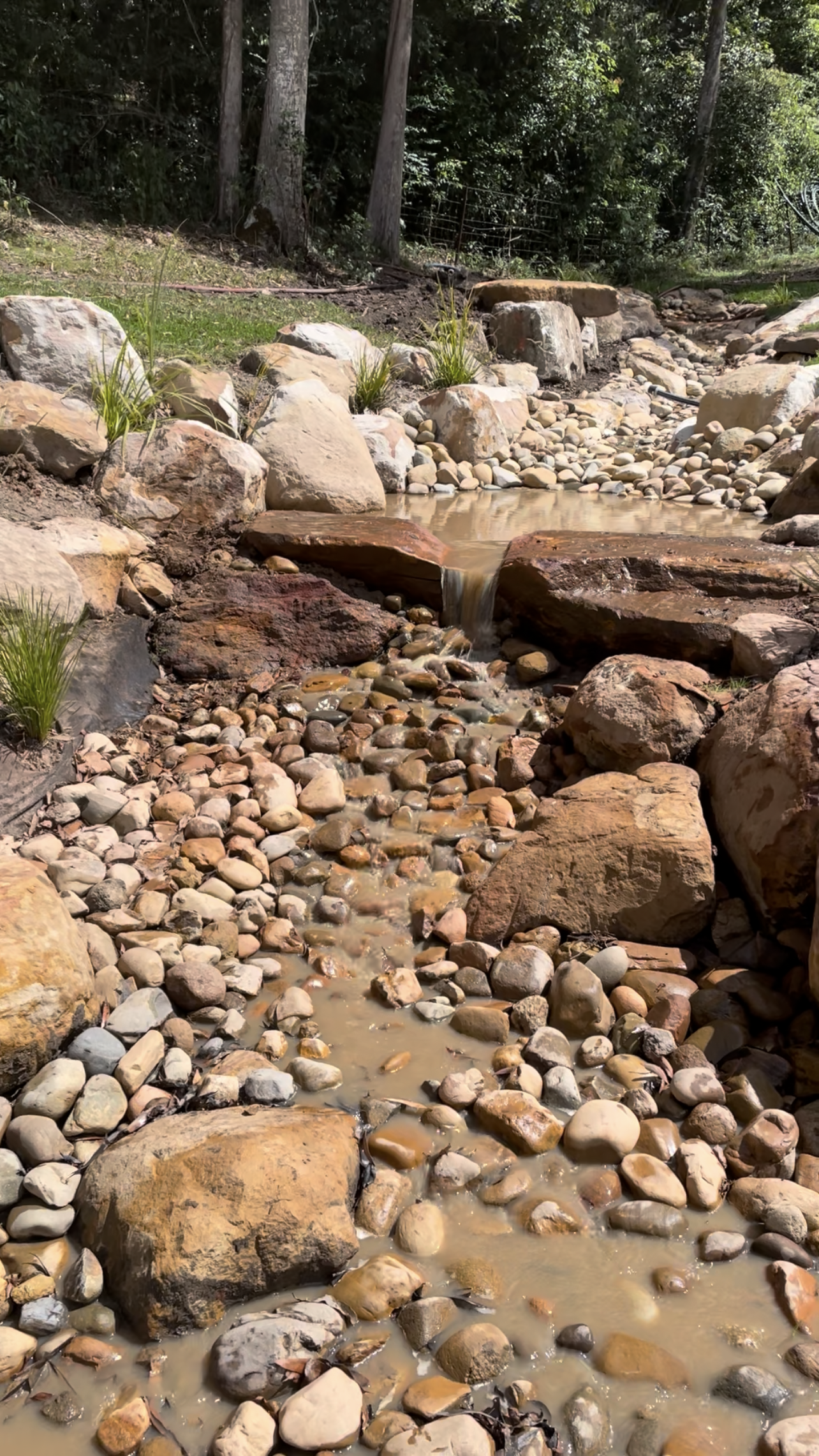 A rocky stream flows between brown rocks in a natural setting.