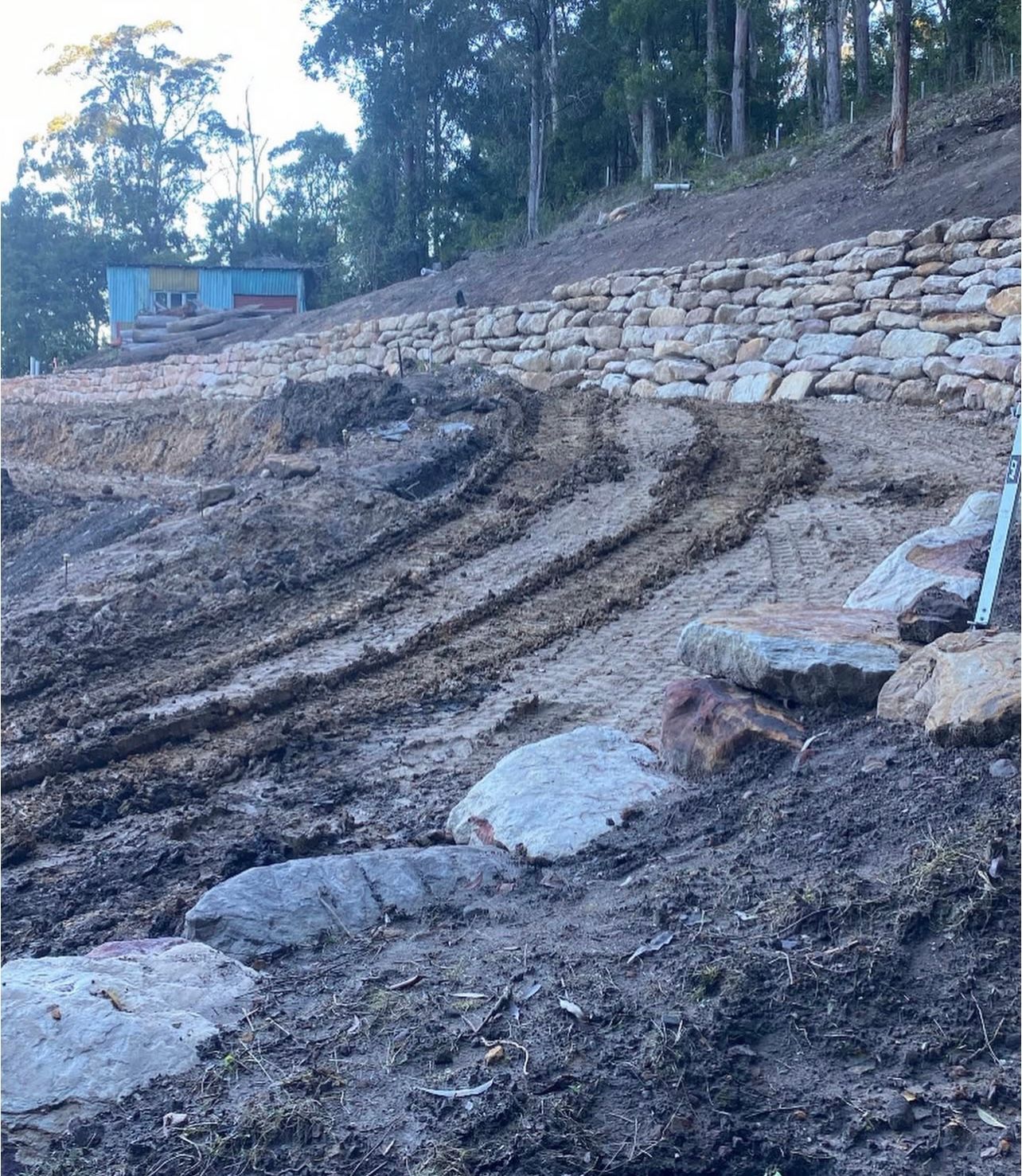 Earthworks project with stone retaining walls and tire tracks on a hillside.