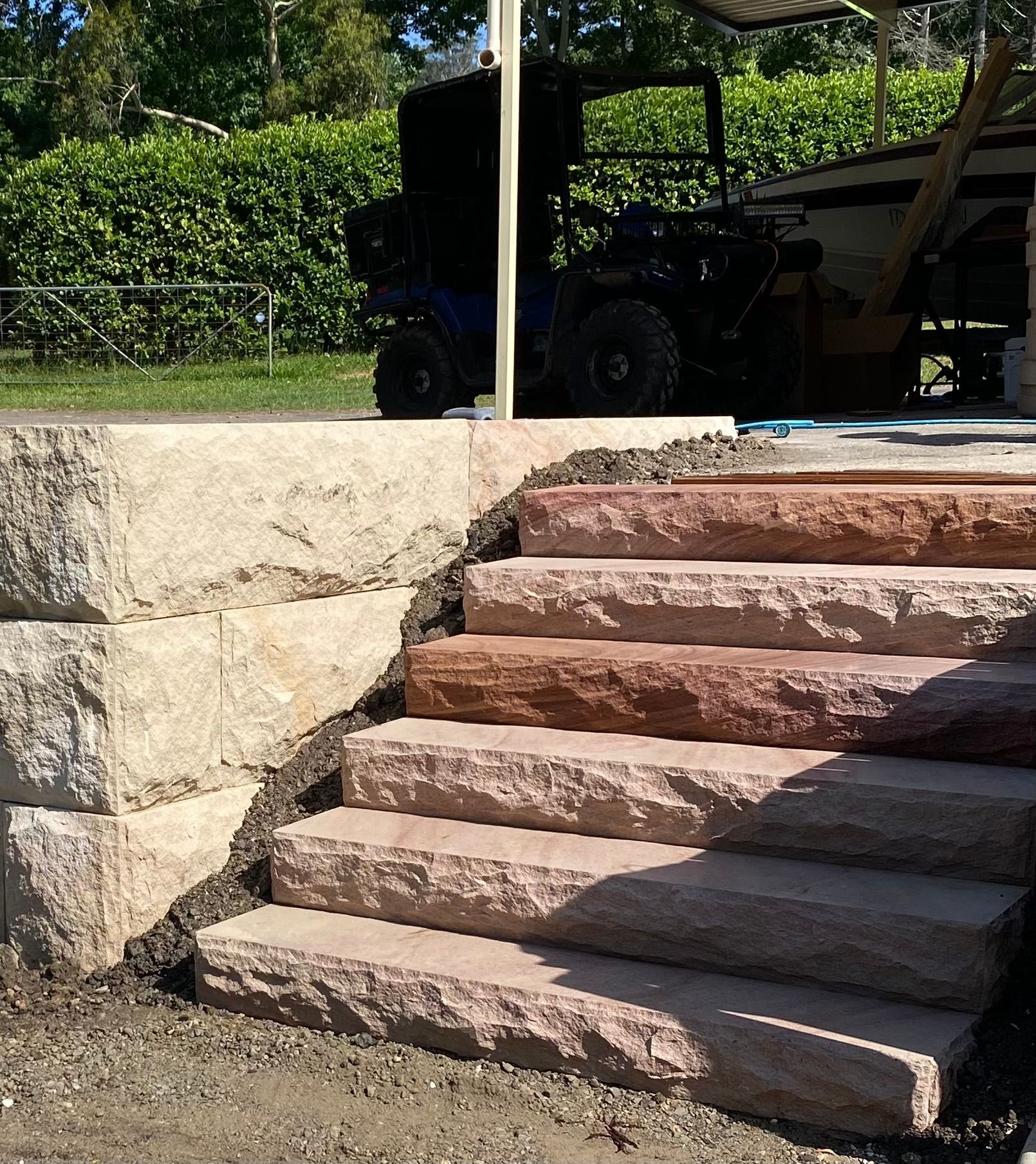 Stone steps and wall leading to a patio with a vehicle parked in the background.
