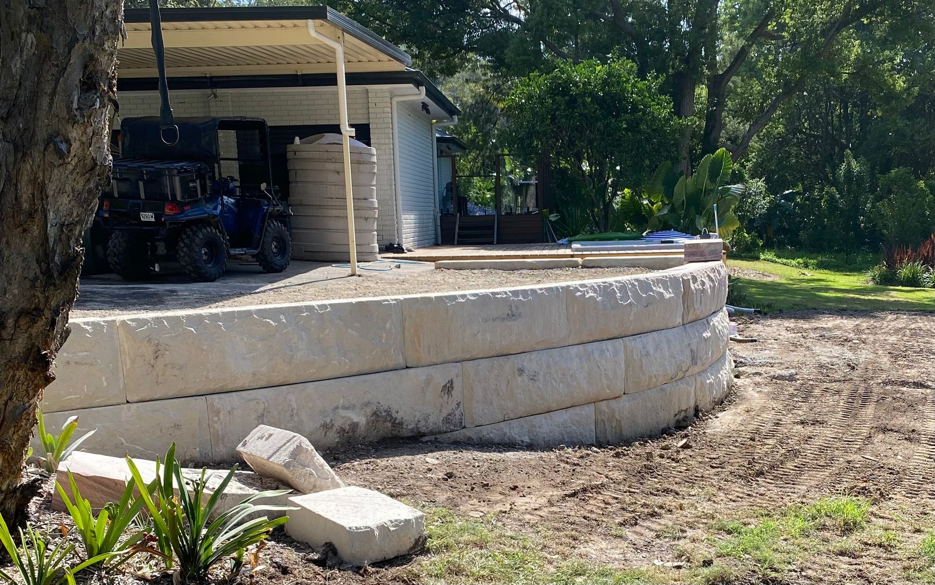 Stone retaining wall under construction next to a house with a four-wheeler parked nearby.