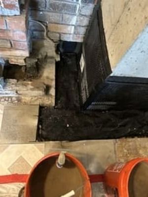 Orange buckets beside a brick fireplace with a dark ash-filled hearth and tiled floor
