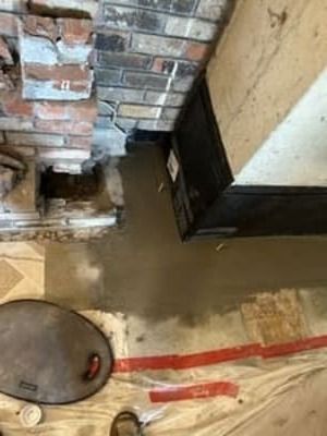 Brick wall with damaged floor and exposed water, plus a round manhole cover and red tape on the ground