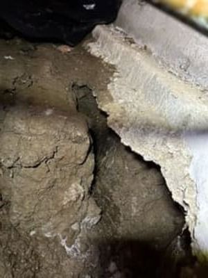 Broken concrete wall with a large hole exposing rough dirt behind it