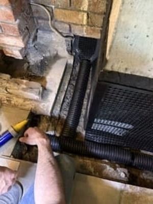 Worker installing black corrugated drainage pipes beside a brick wall and basement opening