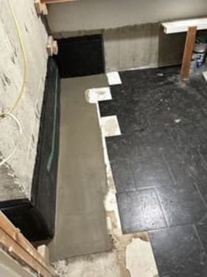 Construction area with a narrow gray concrete strip beside a black tiled floor and exposed wall edges