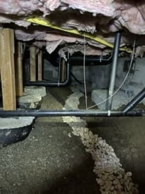Crawlspace under a house with exposed pipes and gravel-covered ground
