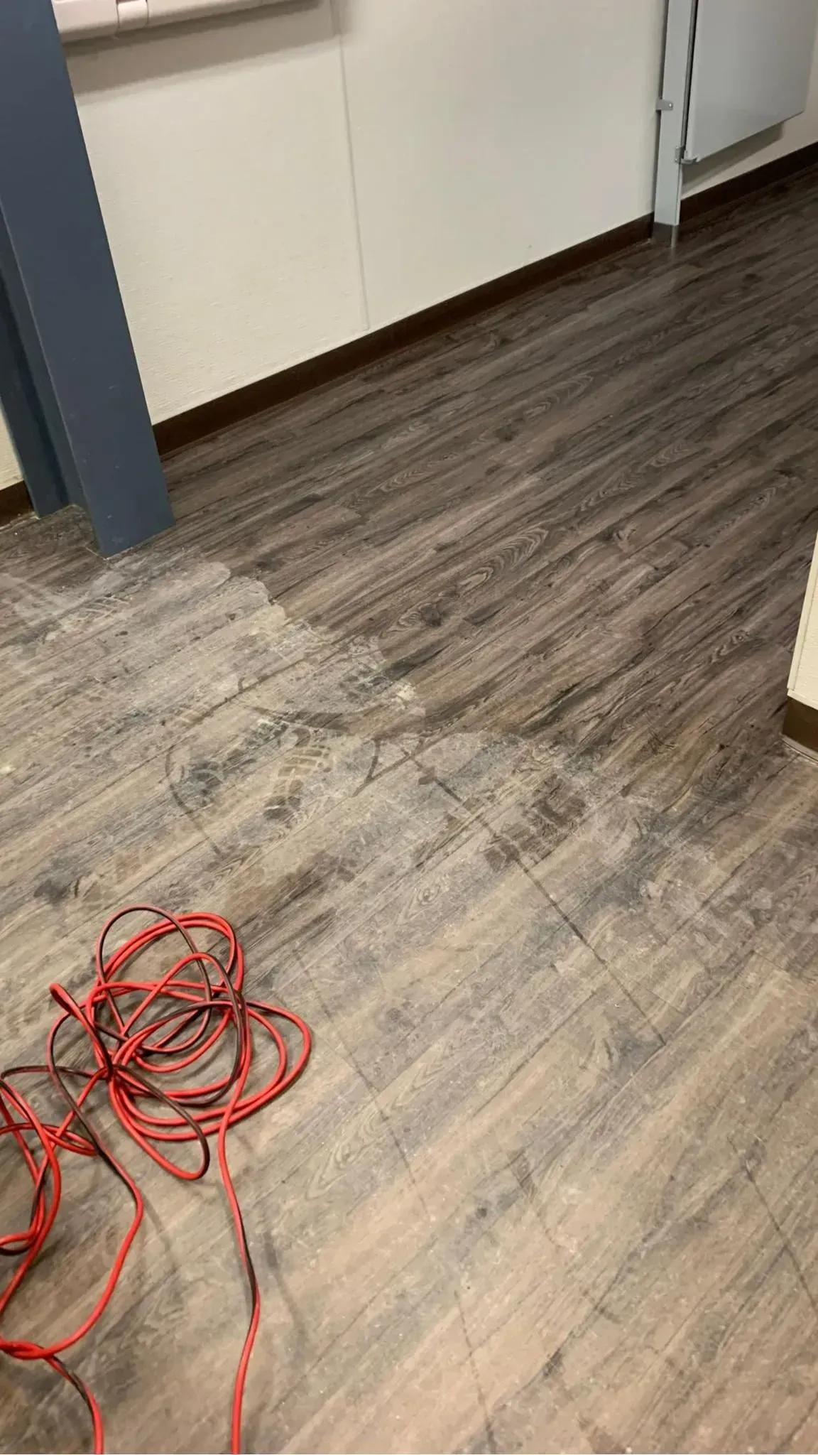 Red extension cord coiled on a worn office floor near white cabinets and a blue door frame.