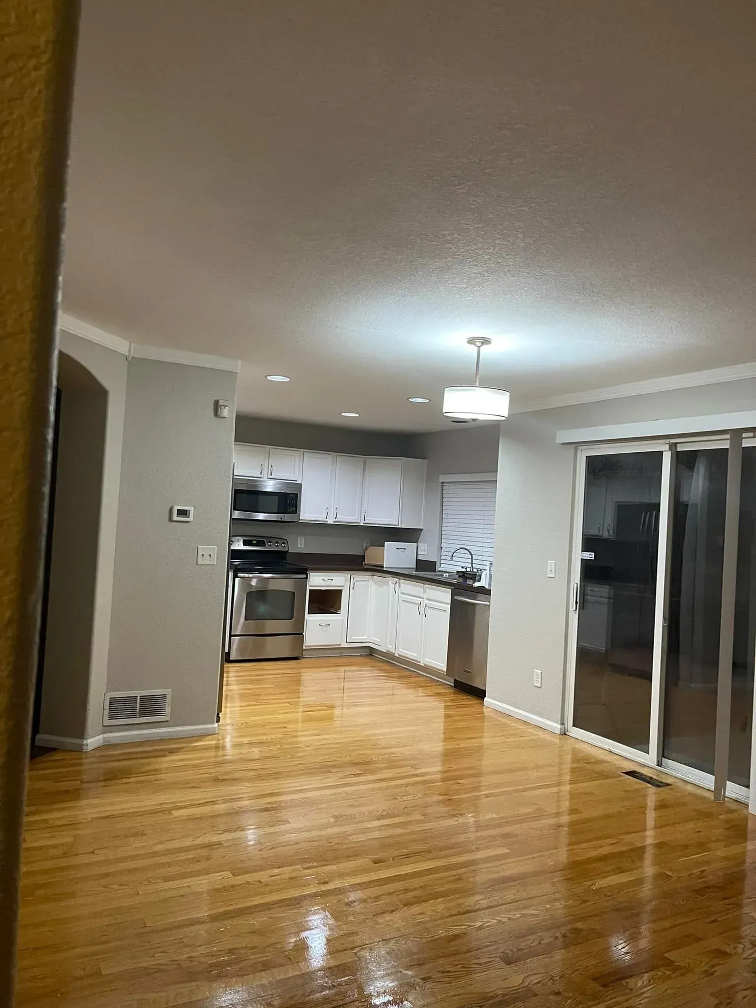 Empty modern living room with glossy wood floors and a small kitchen area in the background