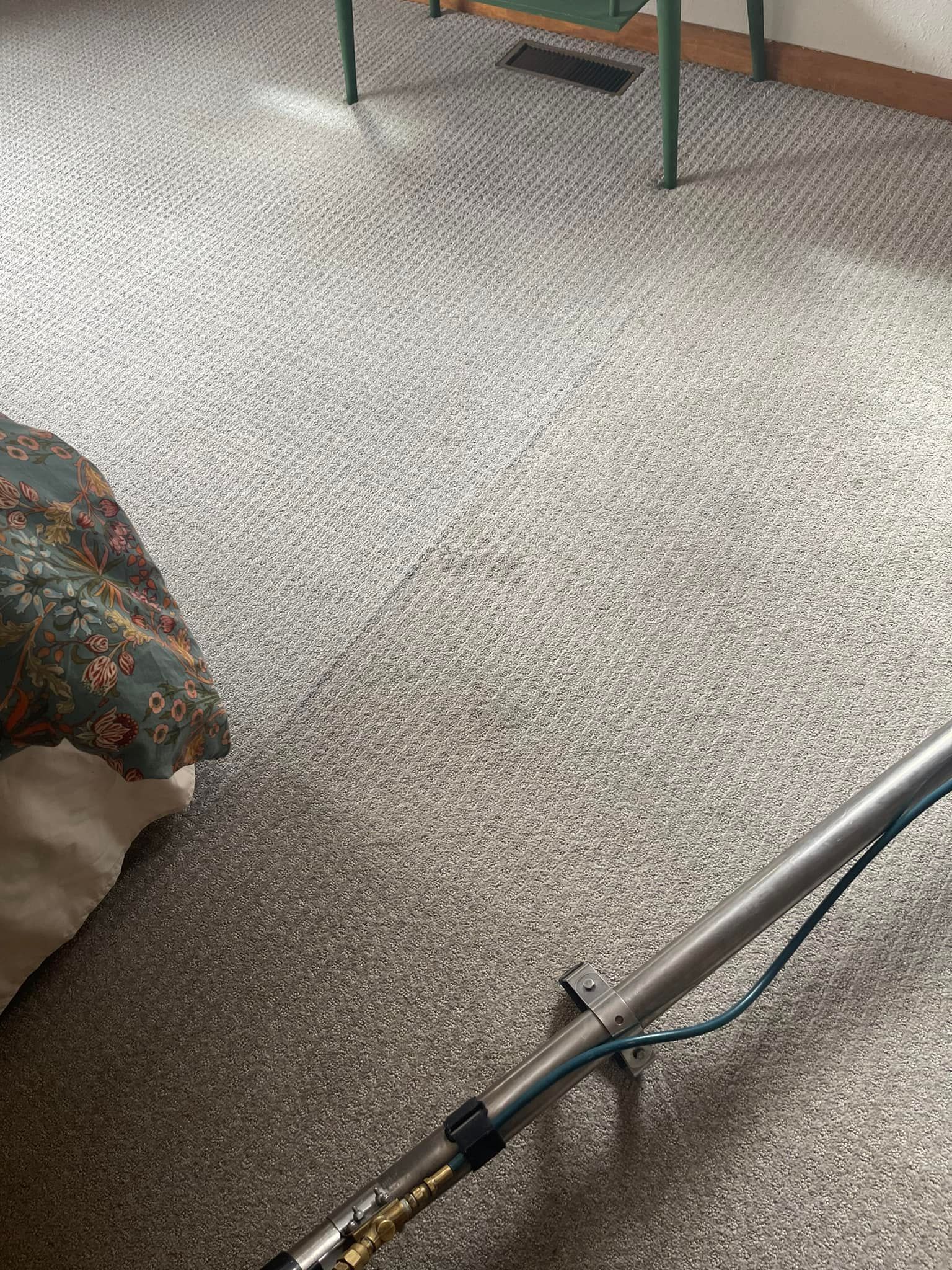 Vacuum cleaner on a speckled carpet beside a floral-covered bed in a room